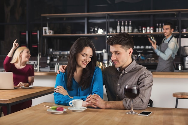 Foto feliz pareja joven tomando café, hablando y sonriendo mientras está sentado en el interior del bar moderno, copie el espacio.