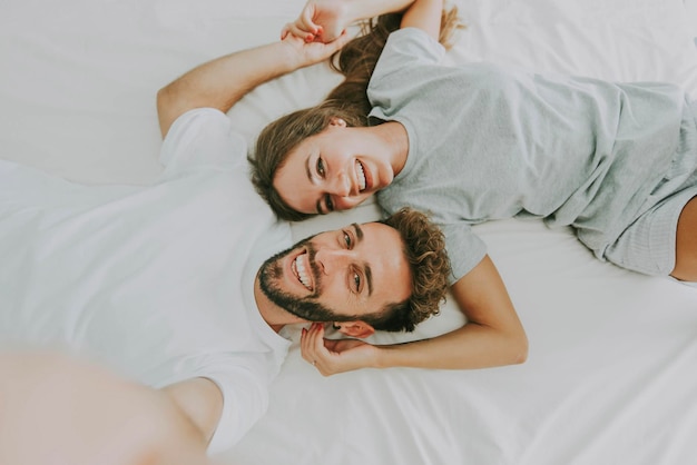 Feliz pareja joven tomando un retrato selfie con un teléfono móvil inteligente acostado en la cama