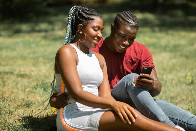 Feliz pareja de jóvenes africanos sentados en el parque en el césped