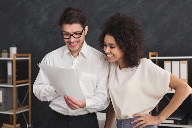 Feliz pareja de jóvenes colegas que trabajan en la oficina moderna. Dos compañeros de trabajo discutiendo su trabajo, trabajando con documentos, señalando en papel, espacio de copia