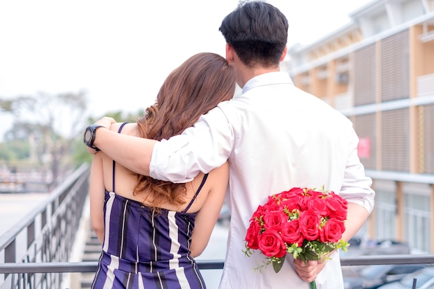 feliz pareja de jóvenes enamorados abrazándose y sosteniendo rosas rojas en las manos de su novia