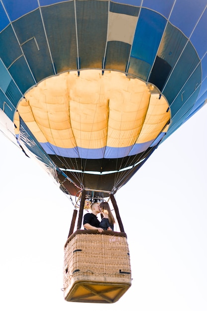 Feliz pareja de jóvenes enamorados besándose en la canasta de globos de aire caliente, mientras disfruta de su primer vuelo