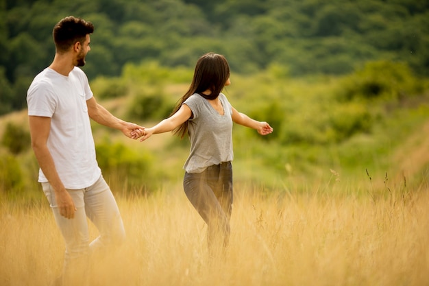 Feliz pareja de jóvenes enamorados caminando por el campo de hierba en un día de verano