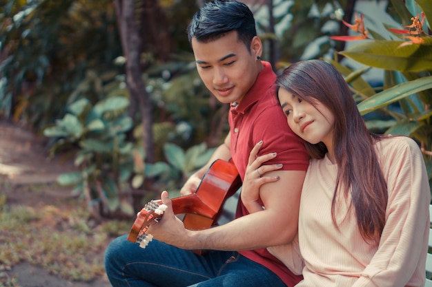 Feliz pareja de jóvenes enamorados sentados en el jardín y tocando la guitarra y cantando.