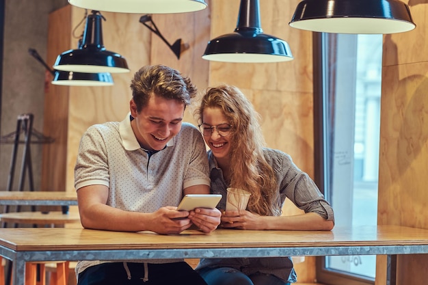 Feliz pareja de jóvenes estudiantes que usan una tableta digital mientras se sientan en una mesa en la cantina de la universidad durante un descanso.