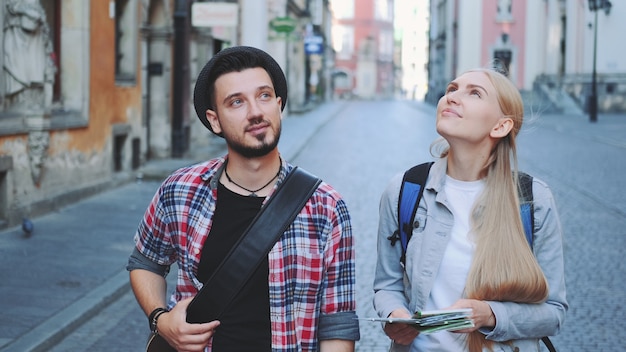 Feliz pareja de jóvenes turistas con mapa caminando y mirando la arquitectura de la ciudad vieja