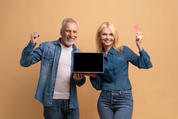Feliz pareja de jubilados usando tarjeta bancaria portátil con pantalla en blanco