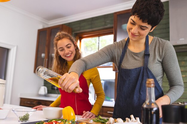 Foto una feliz pareja de lesbianas biraciales cocinando aceite en verduras picadas en la cocina en casa