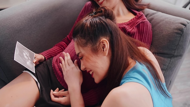 Feliz pareja de lesbianas embarazadas mirando la imagen de ultrasonido juntos en el sofá.