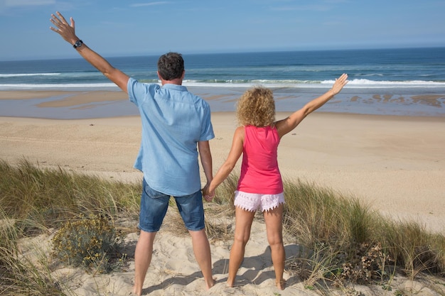 Feliz pareja libre animando en vacaciones de viaje en la playa Vista trasera