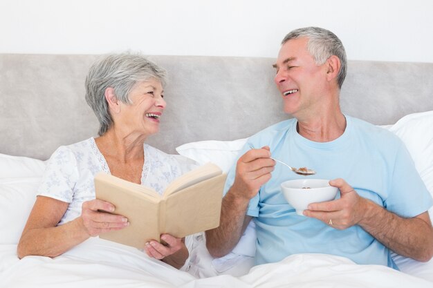 Feliz pareja con libro y tazón de fuente en la cama