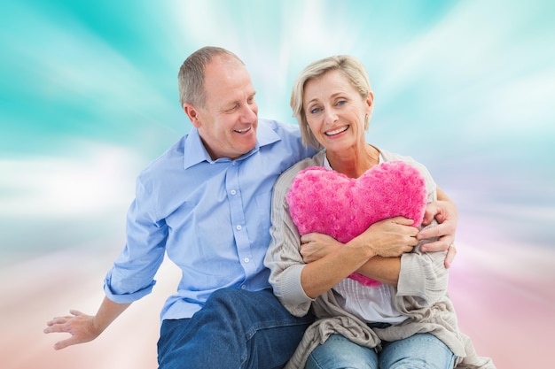 Feliz pareja madura con almohada de corazón contra un diseño femenino rosa y azul generado digitalmente