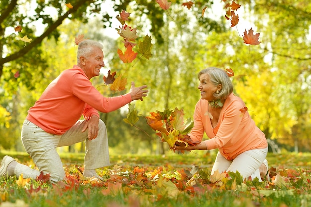 Feliz pareja madura jugar con hojas en el parque otoño