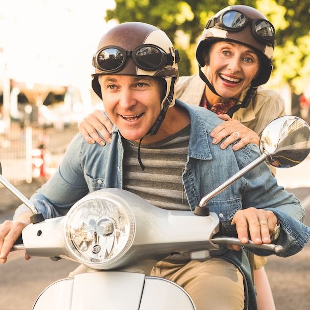 Feliz pareja madura montando un scooter en la ciudad