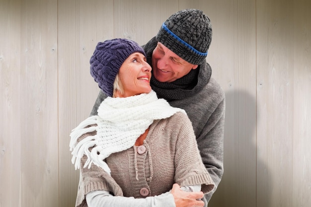 Feliz pareja madura en ropa de invierno abrazándose contra tablones de madera