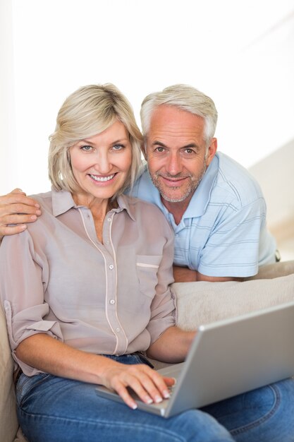 Feliz pareja madura usando la computadora portátil en el sofá