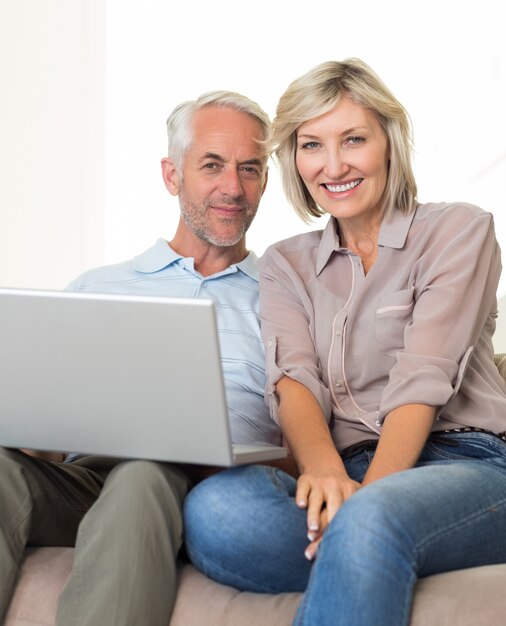 Feliz pareja madura usando la computadora portátil en el sofá