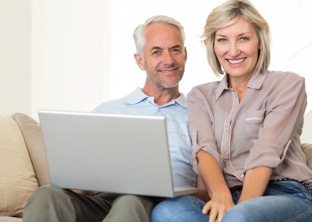 Feliz pareja madura usando la computadora portátil en el sofá