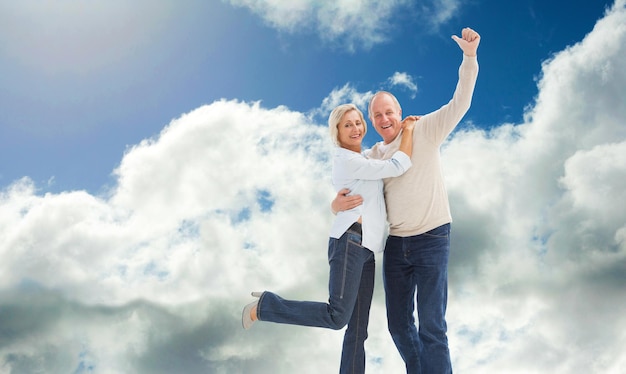 Feliz pareja madura vitoreando a la cámara contra el cielo azul con nubes