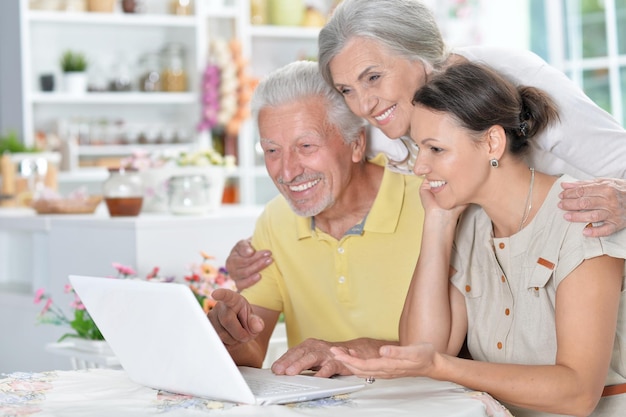 Feliz pareja mayor con hija adulta usando laptop en casa