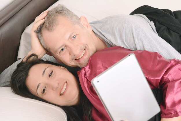 Feliz pareja de mediana edad viendo video en tableta en casa