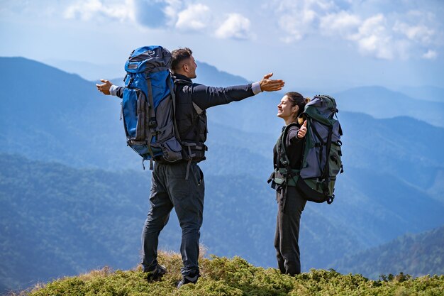 La feliz pareja con mochilas de pie en el fondo del paisaje de montaña