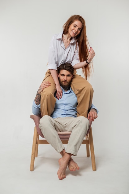 Feliz pareja de moda divertida hermosa mujer alegre sentada sobre los hombros de un tipo brutal hipster en ropa de moda sobre fondo blanco en el estudio