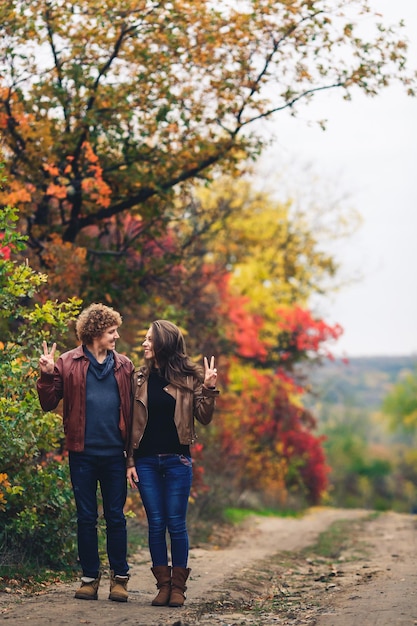 Feliz pareja muestra emociones hombre y mujer en chaquetas de cuero y jeans contra el fondo de árboles de otoño