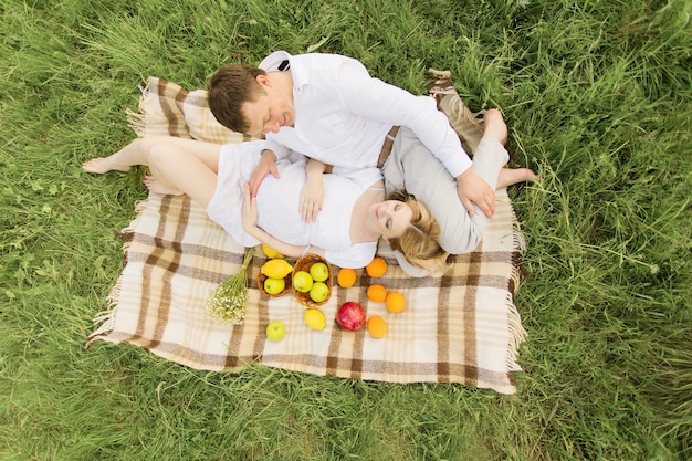 Feliz pareja mujer embarazada y su marido acostado sobre una manta de picnic en la hierba.
