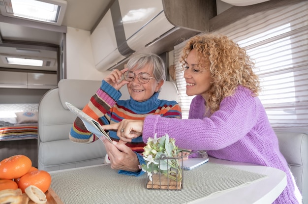 Feliz pareja de mujeres caucásicas sentadas dentro de una autocaravana mirando un mapa planeando viajes