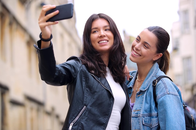 Feliz pareja de mujeres del mismo sexo haciendo turismo mientras posan para Selfie y caminan juntas por Oxford, Reino Unido