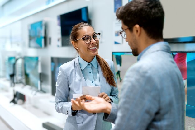 Feliz pareja multicultural en ropa formal hablando sobre el precio del televisor que quieren comprar