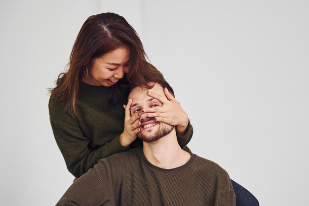 Feliz pareja multiétnica con ropa informal está junta en el interior del estudio. Chico caucásico con novia asiática.