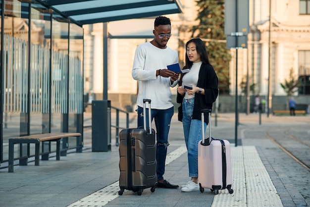 Feliz pareja multirracial mira la tarjeta de embarque comprobando la hora de salida en la parada cerca del aeropuerto. Concepto de viaje de vacaciones.