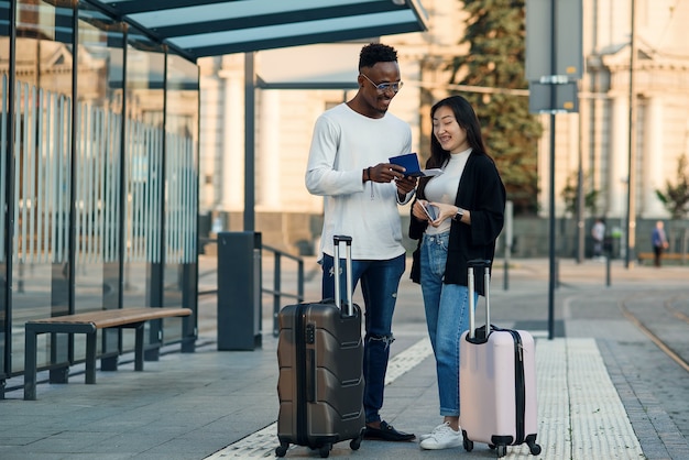 Feliz pareja multirracial mira la tarjeta de embarque comprobando la hora de salida en la parada cerca del aeropuerto.