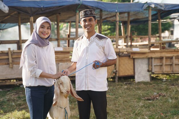 Feliz pareja musulmana compra una cabra para el sacrificio de eid adha o la celebración qurban