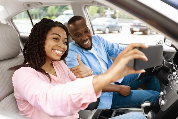 Feliz pareja negra conduciendo coche y tomando selfie en smartphone