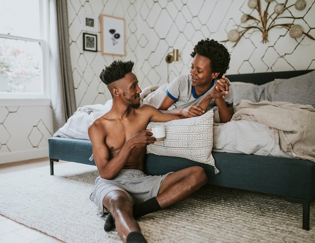 Feliz pareja negra disfrutando de una conversación en la cama mientras bebe café