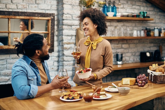 Feliz pareja negra hablando mientras toma una copa de vino en casa