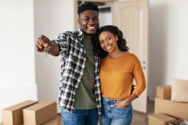 Feliz pareja negra mostrando la nueva llave de la casa abrazándose en casa