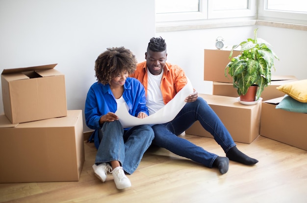Feliz pareja negra planeando la renovación del hogar revisando planos en su nuevo apartamento