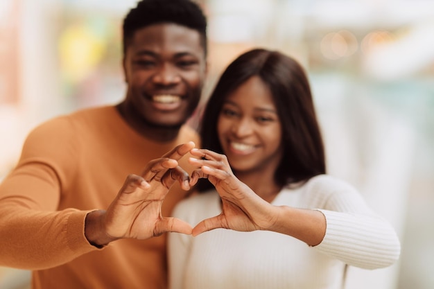 Feliz pareja negra sonriente haciendo forma de corazón con las manos