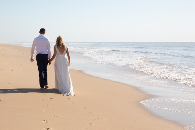 Feliz pareja de novios enamorados en la playa del mar novia y novio en el día del matrimonio en la costa del océano de arena