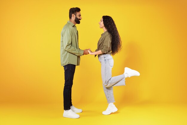 Feliz pareja de oriente medio cogidos de la mano de pie sobre fondo amarillo