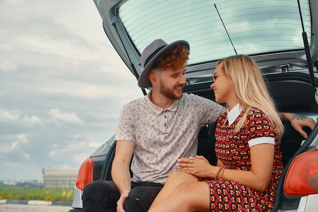 Feliz pareja pasar un buen rato juntos mientras está sentado en el baúl del auto