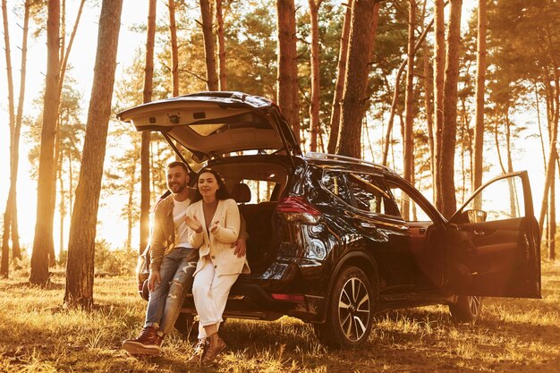 Feliz pareja de pie al aire libre en el bosque con automóvil