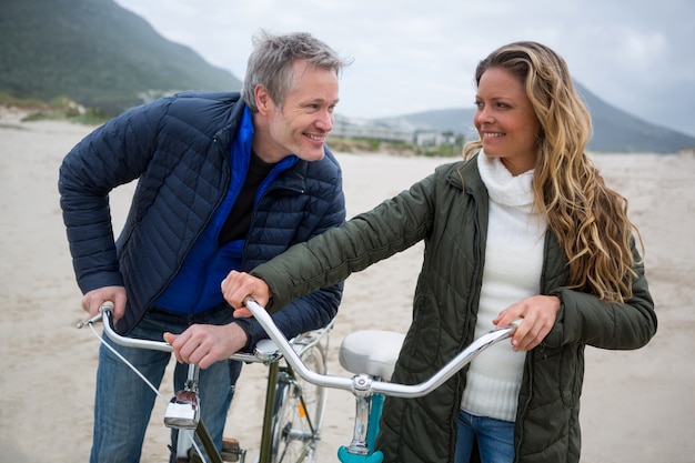 Feliz pareja de pie con bicicleta en la playa