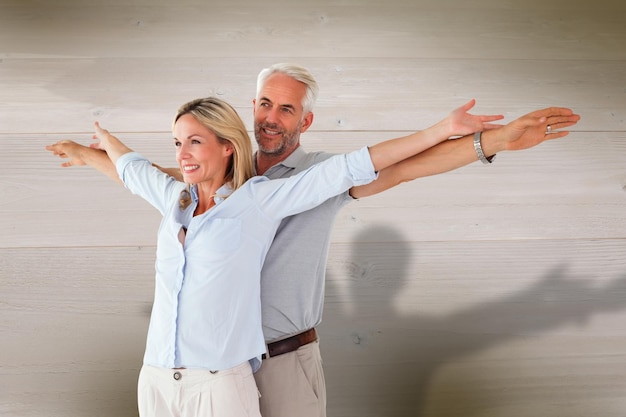 Feliz pareja de pie con los brazos extendidos contra el fondo de tablones de madera blanqueada