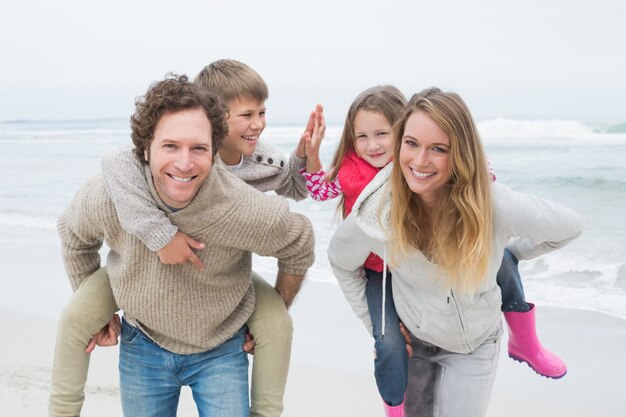 Feliz pareja piggybacking niños en la playa