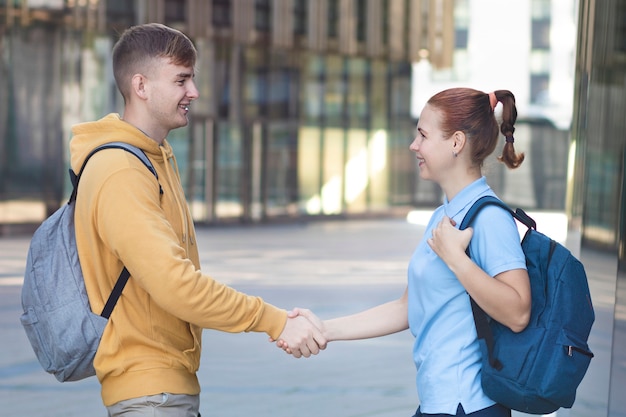 Feliz pareja positiva, dos estudiantes universitarios dándose la mano, de pie con mochilas, sonriendo.